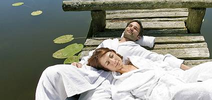 Paar im Bademantel genießt die Sonne auf einem Steg am See