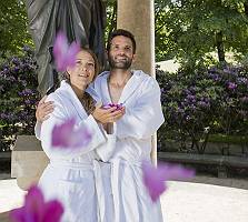Paar im Bademantel steht vor antiker Statue im Blütenregen