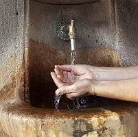 Hände fangen Wasser an altem Trinkbrunnnen auf