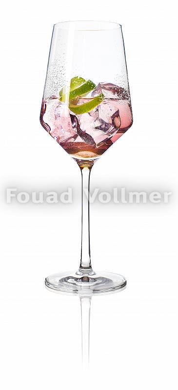 Rosa farbener Aperitif in langstieligem Glas mit Eis und Limette