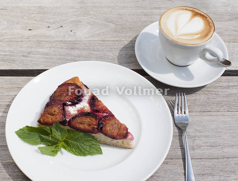 Cappuccino mit Herzschaum auf Holztisch und Zwetschgenkuchen