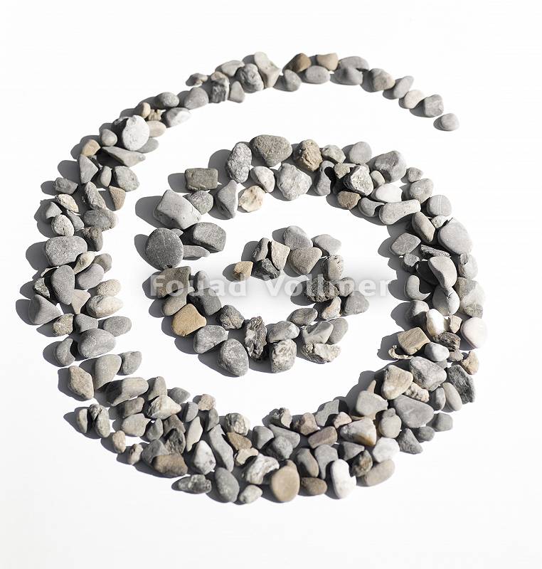 Spirale aus Steinen gelegt auf weißem Untergrund symbolisiert d