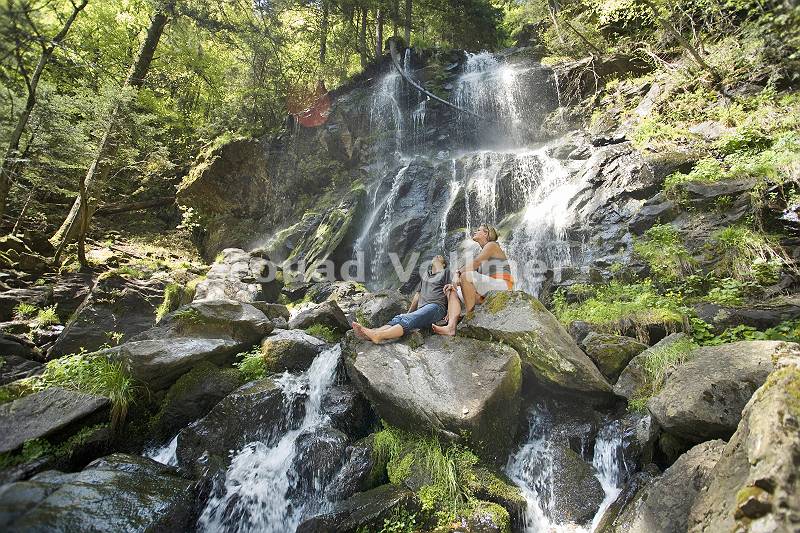 Paar sitzt auf Felsen vor einem Wasserfall und genießt die anre