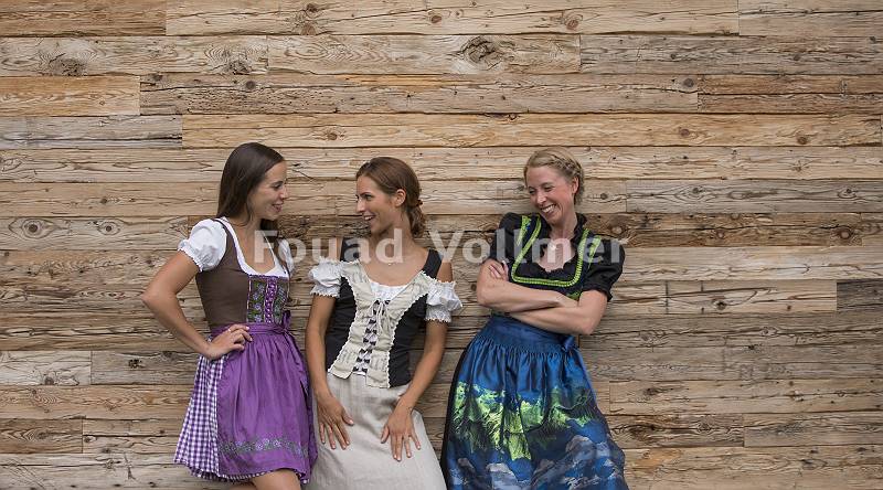 Drei Frauen stehen in Tracht vor einer Holzwand