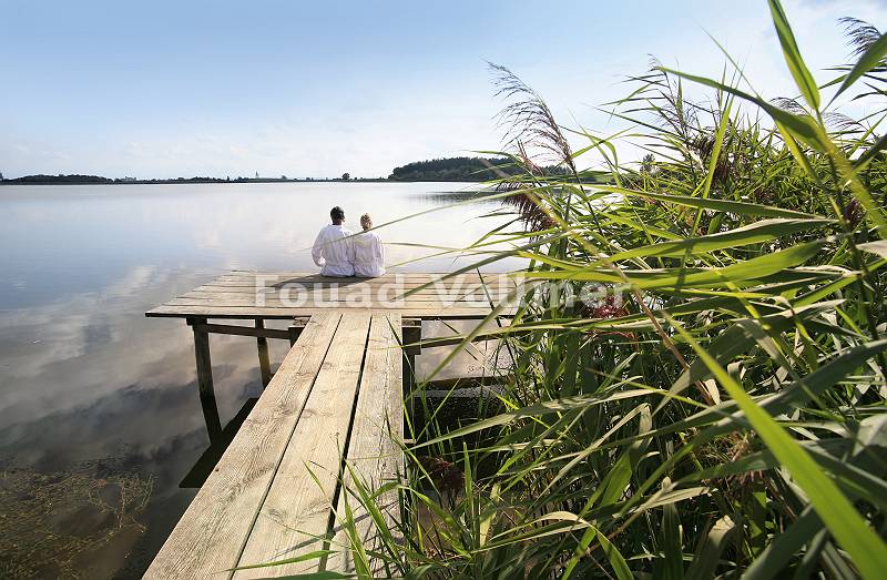 Paar im Bademantel genießt die Sonne auf einem Steg am See