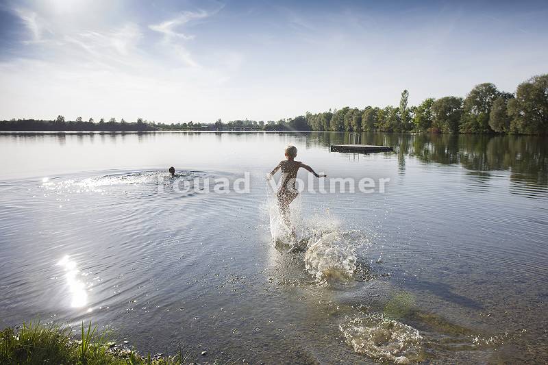 Junge rennt spritzend ins Wasser eines Sees